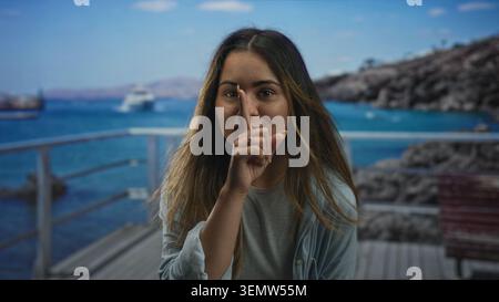 Frau mit offenem Mund auf der Strandpromenade mit Geländer und Boot im Blick; unbeschwertes Vertrauen. Stockfoto
