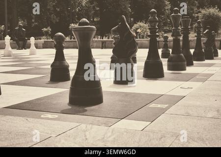Riesiges Freiluftschach, das an einem sonnigen Tag im Kurpark in Polanica Zdroj mit übergroßen schwarzen Stücken auf einem karierten Brett spielt, Sepia-Ton, geringe Tiefe o Stockfoto