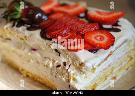 Nahaufnahme eines hausgemachten, mehrschichtigen Biskuittortes mit Sahnefüllung, frischen Erdbeerscheiben und Schokoladengläsern. Weiche flache Schärfentiefe und W Stockfoto