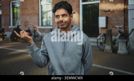 Mann in grauem Kapuzenpullover zeigt mit dem Finger auf den Tempel auf der Kopfsteinpflasterstraße neben geparkten Fahrrädern und Backsteintüren; nachdenklich. Stockfoto