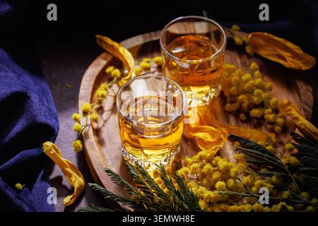 Zwei Gläser Whiskey oder Brandy mit Mimosa-Blumen auf Holztablett Frühlingsfeierungs-Getränk Stockfoto