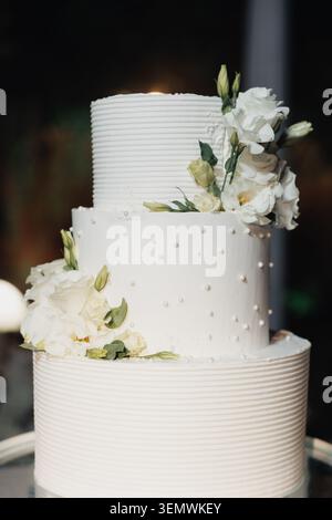 Weiße Kuchenschichten zeigen eine elegante Textur. Blumenakzente sorgen für ein weiches, romantisches Detail. Perlfarbene Punkte schmücken die mittlere Ebene. Die sanfte Beleuchtung hebt die Torten hervor Stockfoto