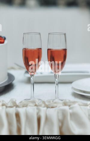Zwei Gläser Rosenwein stehen elegant nebeneinander. Die weiße Tischdecke fällt sanft unter sie. Die zarten Stiele reflektieren die des Umgebungslichts Stockfoto
