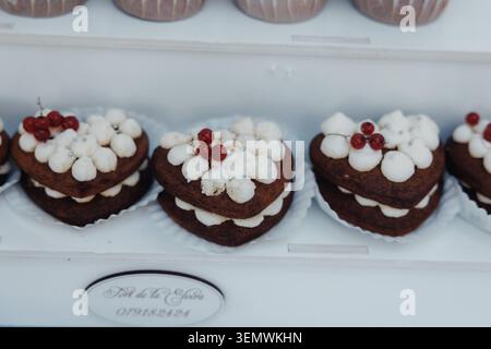 Herzförmige Schokoladenkuchen mit Marshmallows und roten Beeren. Weißes Tablett für süße, festliche Leckereien. Elegante Präsentation perfekt für Feiern. Stockfoto
