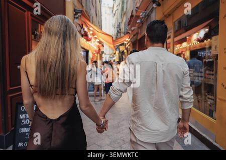 Ein paar spazieren Hand in Hand durch eine bezaubernde Gasse. Warme Töne erstrahlen von den Geschäften und Laternen in der Nähe. Sie bewegen sich mit ruhiger Zufriedenheit, die Köpfe rutschen Stockfoto