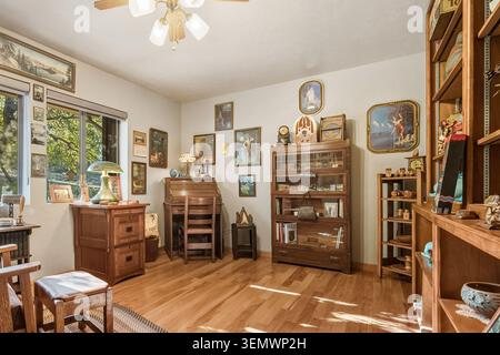 Ein sonnendurchflutetes Wohnzimmer mit antiken Holzmöbeln, Regalen, gerahmten Gemälden, einem Deckenventilator und warmen Hartholzböden, die eine nostalgische Ho schaffen Stockfoto