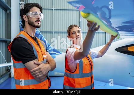 Luftfahrtingenieure mit Sicherheitswesten und -Brille überprüfen einen Flugzeugflügel in einem Hangar akribisch und vertreten Teamwork, Sicherheit und Professi Stockfoto
