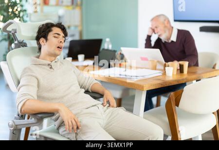 Müde ältere und junge männliche Kollegen schlafen während der Arbeit ein Stockfoto