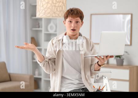 Schockierter junger Mann, der zu Hause mit Laptop arbeitet Stockfoto