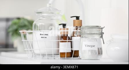 Umweltfreundliche Haushaltsreinigungszubehör: Natron, Essig und natürliche Seifen in einem minimalistischen weißen Korb Stockfoto