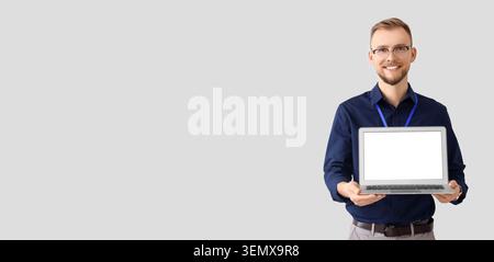 Lächelnder junger Mann, der Laptop mit leerem Bildschirm, Geschäftspräsentation und Technologiekonzept hält, isoliert auf grauem Hintergrund Stockfoto