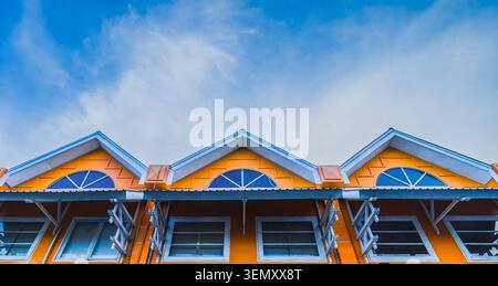Eine flache, symmetrische Aufnahme von drei hellorangefarbenen Ladengebäudeoberflächen mit dreieckigen Dächern und Bogenfenstern. Stockfoto