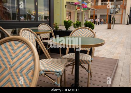 Großer Blick auf eine moderne Restaurantterrasse mit leeren grünen Tischen und gewebten Bistrostühlen auf einem Bürgersteig Stockfoto