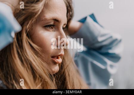 Frau Profil Porträt Frau passt ihr langes blondes Haar in weichem natürlichem Licht im Freien an und zeigt nachdenklichen Ausdruck und klare Haut Stockfoto