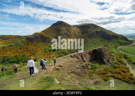 Menschen, die über den Gipfel der Salisbury Crags laufen, mit Arthurs Seat im Hintergrund, Holyrood Park, Edinburgh, Schottland Stockfoto