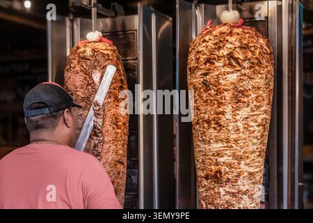 Restaurantarbeiter bereiten Shawarma und Döner auf vertikalem Grill in der Fast-Food-Küche zu. Das Bild zeigt das Schneiden von geröstetem Fleisch auf r Stockfoto