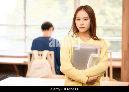 Ernsthafte junge japanische Studentin, die ein digitales Gerät und Bücher in einem Café hält Stockfoto