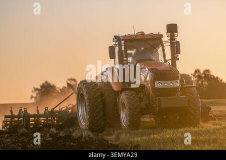 Traktor mit Bodenbearbeitungsausrüstung, der während der Bodenbearbeitung und des Pflügens auf landwirtschaftlichen Flächen arbeitet. Bodenvorbereitung für die Aussaat, maschinelle Landwirtschaft, Landwirtschaft Stockfoto