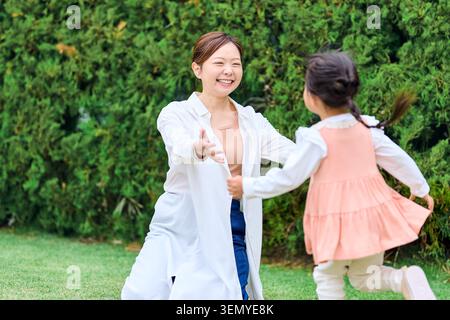 Glückliche japanische Mutter und Tochter spielen draußen auf grünem Gras zusammen Stockfoto