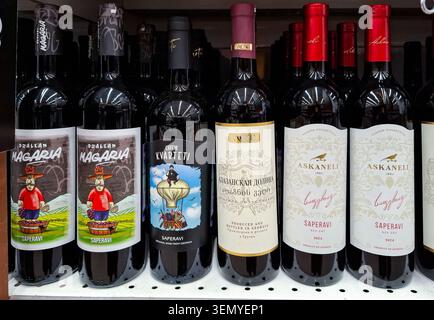 Woronesch, Russland - 11. April 2026. Mehrere Flaschen georgianischen Rotweins säumen das Regal in einem Supermarkt. Die Etiketten sind mit Cartoon-Designs versehen. Käufer c Stockfoto