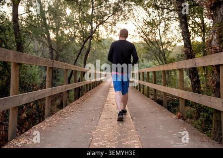 Mann, der auf einer langen Holzbrücke trainiert, umgeben von Bäumen und Laub Stockfoto
