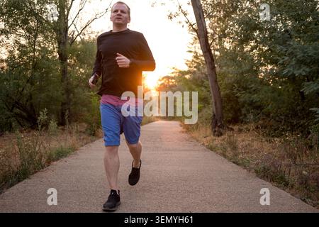 Mann läuft auf einem gepflasterten Weg zur goldenen Stunde, symbolisiert Gesundheit und aktiven Lebensstil Stockfoto