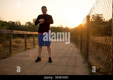 Mann überprüft Fitness-Tracker am Handgelenk während eines Outdoor-Workouts zur goldenen Stunde Stockfoto
