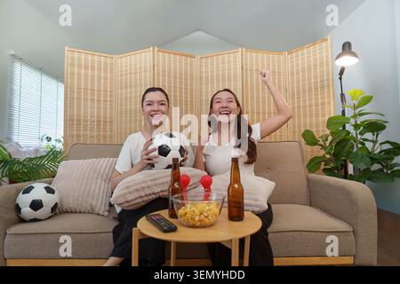 Glückliche asiatische Frauen, die zuhause beim Fußballspiel anfeuern Stockfoto