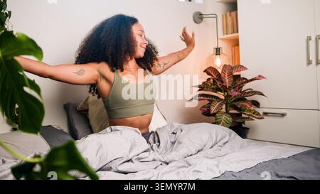 Schwarze Frau dehnt sich in gemütlichem, modernem Schlafzimmer im Morgenlicht, glücklich und entspannt Stockfoto