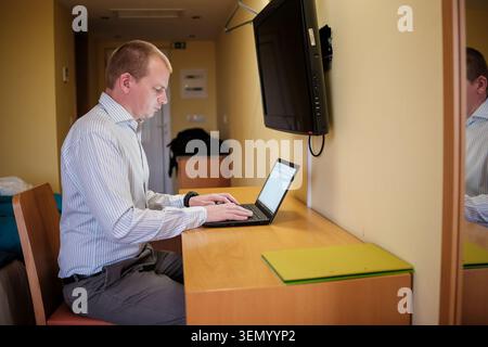 Geschäftsmann, der sich auf Laptop konzentriert, während einer Geschäftsreise in einem Hotelzimmer aus der Ferne arbeitet Stockfoto