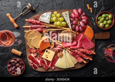 Antipasti oder Tapas. Wurst- und Käsebrett mit Wein, von oben auf schwarzem Steingrund geschossen. Mediterrane Speisen und Getränke Stockfoto