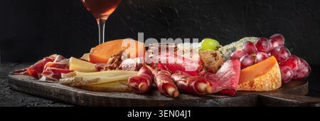 Antipasti- oder Tapas-Panorama. Wurst- und Käseplatte. Spanische und italienische Gourmetgerichte und -Getränke auf Schwarz Stockfoto