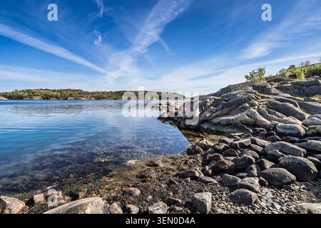 Ruhige Küstenszene mit glatten Felsen, ruhigem Wasser und natürlicher Vegetation unter einem hellblauen Himmel Stockfoto