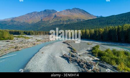 Ein sich windender Fluss fließt durch einen Wald mit Bergen im Hintergrund unter einem klaren blauen Himmel. Moose Pass, Alaska, USA Stockfoto