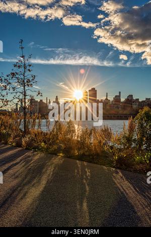 Sonnenuntergang hinter einer Skyline der Stadt, die lange Schatten an einem malerischen Flussweg wirft. New York, USA Stockfoto