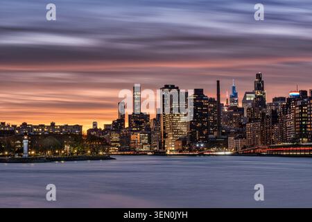 Atemberaubende Skyline der Stadt in der Abenddämmerung mit lebhaften Sonnenuntergang über der ruhigen Uferpromenade. New York, USA Stockfoto