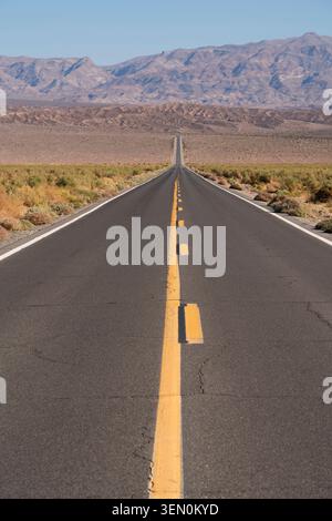 Gerade leere Straße führt zu fernen Bergen unter einem klaren blauen Himmel in einer Wüstenlandschaft. Stockfoto