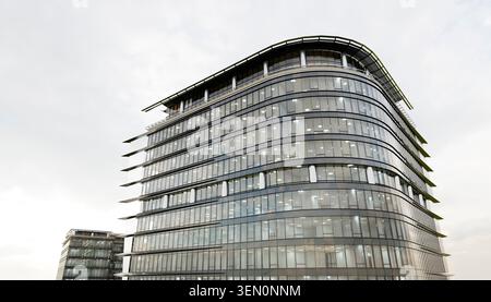 Modernes Bürogebäude aus Glas mit geschwungener Fassade unter bewölktem Himmel. Abbildung, Rendering Stockfoto