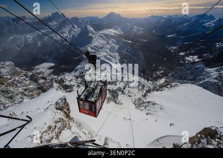 Eine rote Seilbahn steigt bei Sonnenuntergang über eine schneebedeckte Berglandschaft auf. Stockfoto