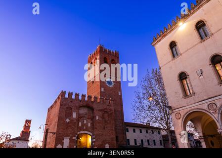 Historischer Backsteinglockenturm und bogenförmige Gebäude unter klarem Abendhimmel in einer italienischen Stadt. Stockfoto