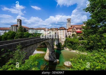 Steinbrücke über einen klaren türkisfarbenen Fluss mit farbenfrohen historischen Gebäuden und einer üppigen Landschaft. Stockfoto