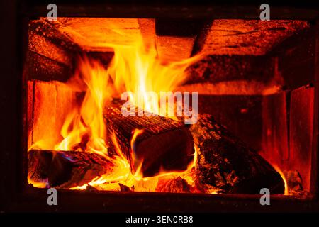 In einem gemütlichen, rustikalen Kamin tanzen helle Flammen um Baumstämme. Stockfoto