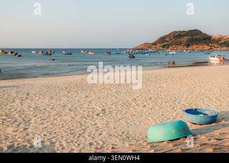 Sandstrand mit Fischerbooten auf dem Meer und Hügeln im Hintergrund unter klarem Himmel. Stockfoto