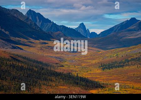 Majestätische Bergkette mit farbenfrohem Herbsttal unter teilweise bewölktem Himmel. Stockfoto