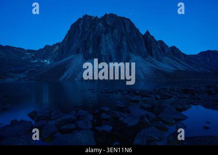 Majestätische Bergsilhouette vor einem tiefblauen Himmel, der sich in einem ruhigen See in der Abenddämmerung spiegelt. Stockfoto