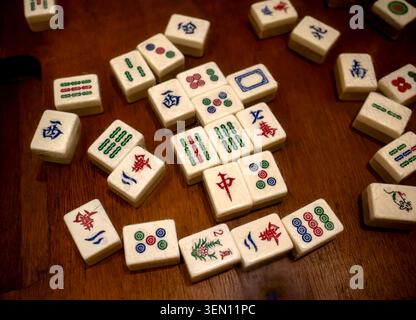 Große Nahaufnahme traditioneller chinesischer Mahjong-Fliesen, die auf einer hölzernen Tischfläche verstreut sind Stockfoto