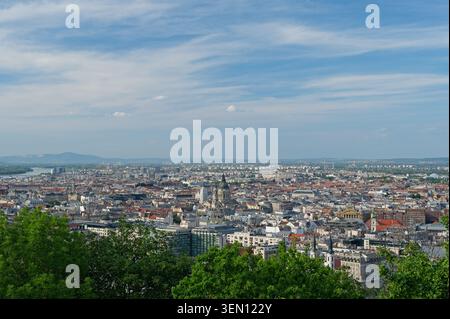 Budapest, Ungarn - 31. Mai 2026: Weites Panorama der dichten Skyline der Stadt Pest mit dem Stephansdom, Blick vom Gellert-Hügel über grünen Bäumen. Stockfoto