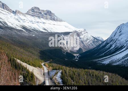 Schneebedeckte Bergkette mit gewundenen, waldgesäumten Straßen unter klarem Himmel. Stockfoto