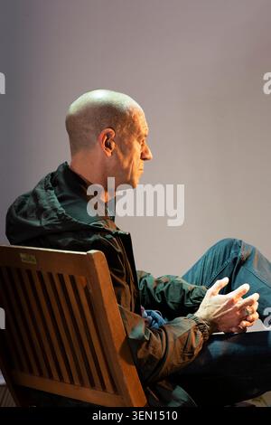 Diarmaid Ferriter sitzt auf einem hölzernen Stuhl, die Hände sind zusammengeschlossen. . Das Porträt ist orange und grün beleuchtet, wie die Farben der irischen Flagge Stockfoto