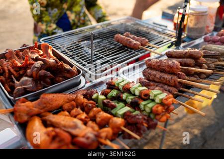 Verschiedene gegrillte Fleischgerichte und Gemüse auf Spießen, die auf einem Street Food Grill gekocht werden. Stockfoto